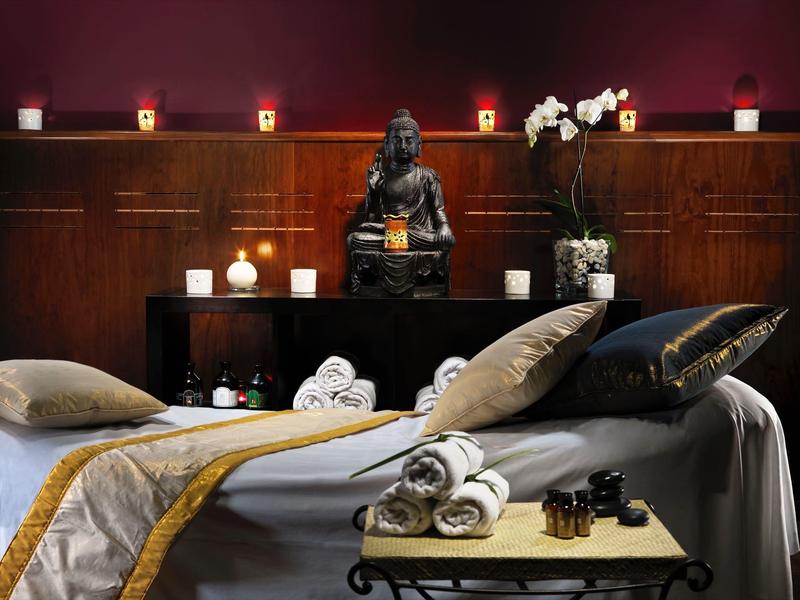 Luxury spa room with a Buddha statue, candles, orchids, and a massage table.