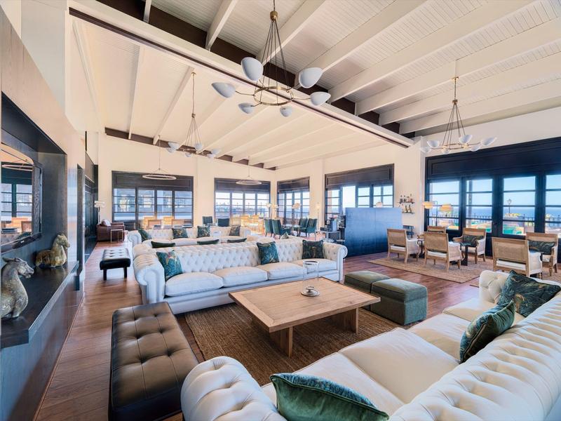 Spacious hotel lounge with modern sofas, large windows, and a wooden beamed ceiling.