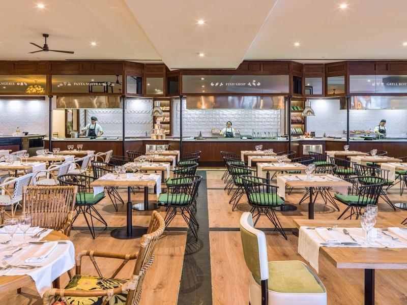 Spacious hotel restaurant with neatly arranged tables, green chairs, and wooden flooring.