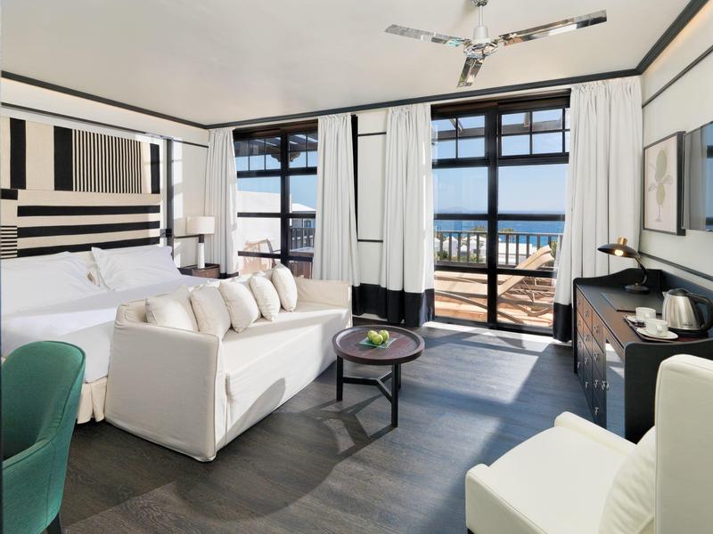 Modern hotel room with ocean view, white and black decor, and comfortable seating.