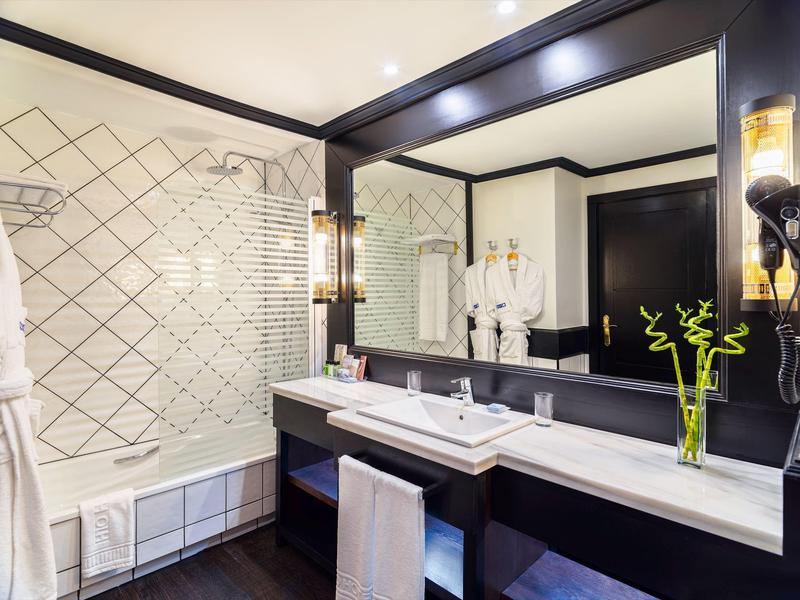 Modern bathroom with large mirror, double sink, bathtub, and white tiled wall with pattern.