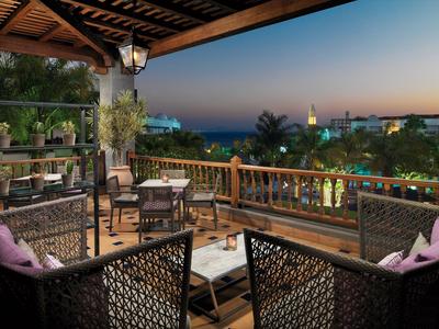 Terrassenbereich mit Stühlen, Tischen, Pflanzen und Blick auf Meer und Abendhimmel.