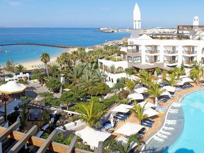 Hotelanlage mit großem Pool, Palmen, Liegestühlen und Blick auf das blaue Meer und den Strand.