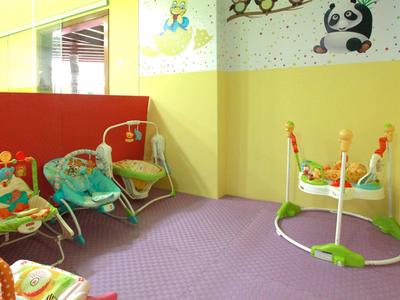 Kinderspielecke mit bunten Schaukelsitzen, weichem lila Teppich und gelb-grünen Wänden.