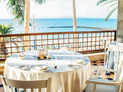 Terrassen-Tisch mit weißer Tischdecke, gedeckt mit Geschirr, Blick auf Meer und Palmen.