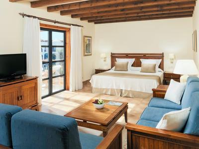 Světý hotelový pokoj s nábytkem ze dřeva, dvě modré pohovky a velká postel