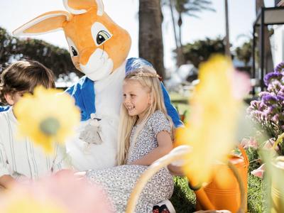 Enfants avec une mascotte de kangourou entourés de fleurs en plein air par temps ensoleillé.