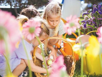 Des enfants cueillent des fleurs dans un jardin ensoleillé avec des fleurs colorées.