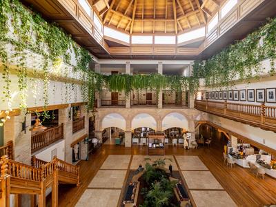 Velký hotelový interiér s dřevěnými stropy, zelenými rostlinami a posezením.