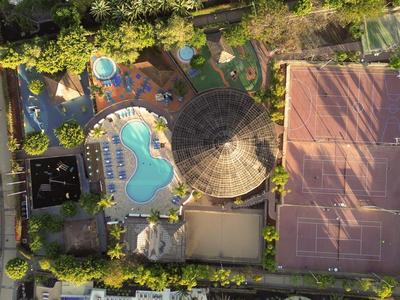 Vue aérienne d'un complexe hôtelier avec piscine, terrain de tennis et pavillon ombragé.