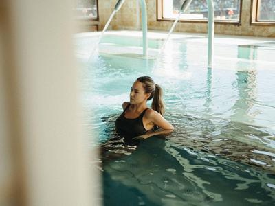 Žena relaxuje v hotelovém krytém bazénu s fontánami a přirozeným světlem.