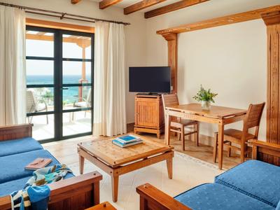 Pohodlný obývací pokoj s dřevěným nábytkem, dvěma modrými pohovkami a výhledem na moře.