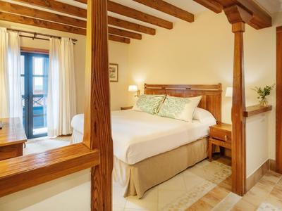 Pohodlná ložnice s dřevěnými trámy, velkými okny a neutrálním dekorem.