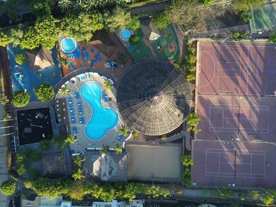 Letecký pohled na hotel s bazénem, tenisovým kurtem a okolní zelení.