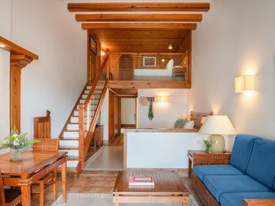 Pohodlný obývací prostor s dřevěným stropem, modrou pohovkou, jídelním stolem a schody na galerii.