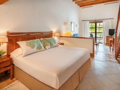 Pohodlný hotelový pokoj s manželskou postelí, nočními stolky, otevřenou koupelnou a přístupem na balkon.