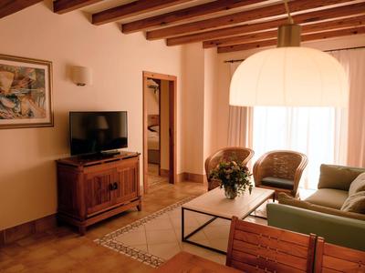 Pohodlný obývací pokoj s dřevěnými trámy, pohovkou, křesly a nízkým stolkem s květinami.