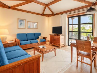 Světý obývací pokoj s modrými pohovkami, dřevěným nábytkem a balkónem s výhledem na moře.