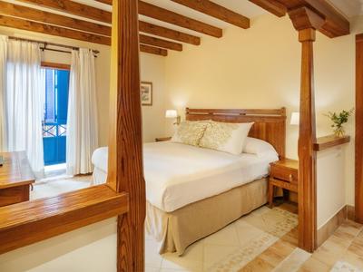 Světý hotelový pokoj s dřevěnými trámy, velkou postelí a balkonem s výhledem na moře.