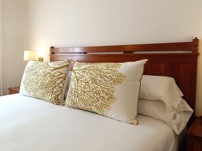 Pohodlná postel s bílým povlečením a dekorativními polštáři u dřevěného čela postele.