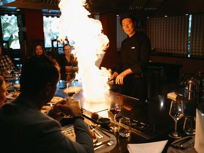 Restaurant mit Gästen, die an einem Tisch sitzen, während ein Kellner eine Flamme erzeugt.