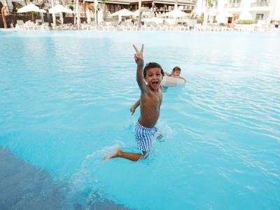 Zwei Kinder springen und spielen fröhlich im klaren blauen Hotelpool.