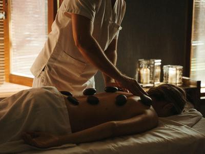 Person erhält Hot-Stone-Massage in ruhigem, gedämpftem Raum mit natürlichem Licht.