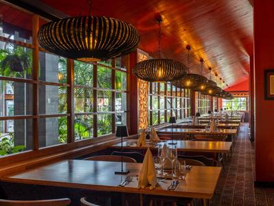 Hotelrestaurant mit Holztischen, großen Fenstern und moderner Beleuchtung.