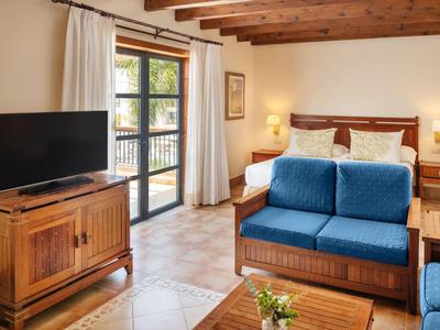 Helles Hotelzimmer mit Holzdecke, blauem Sofa, TV und Bett mit weißen Kissen.
