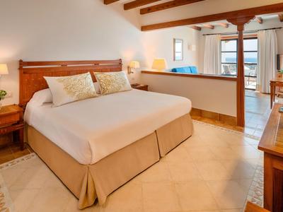 Helles Hotelzimmer mit großem Doppelbett, Holzmöbeln und Blick auf den Balkon.
