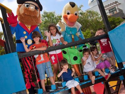 Kinder spielen auf einem bunten Klettergerüst mit großen Piratenfiguren im Freien bei Sonnenschein.