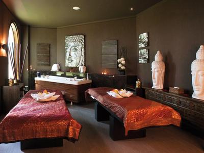 Pokojová spa místnost se dvěma masážními stoly, dekorativními sochami a teplým osvětlením.