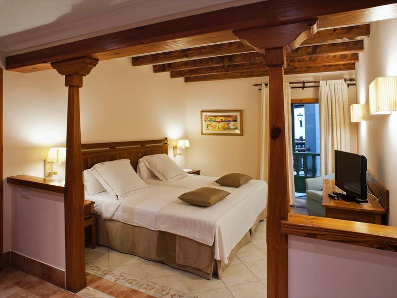 Chambre d'hôtel confortable avec lit double, plafond aux poutres en bois et télévision.
