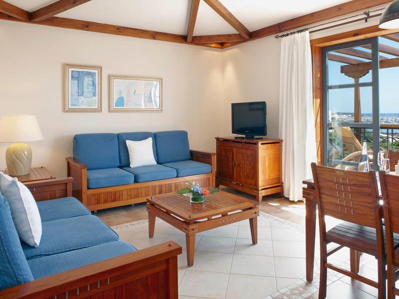 Salon lumineux avec meubles en bois, canapés et vue sur la mer par des portes coulissantes en verre.