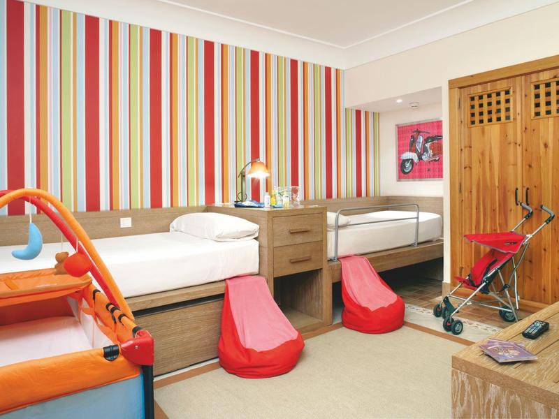 Chambre d'hôtel avec deux lits simples, motif mural rayé coloré et rehausseurs pour enfants.
