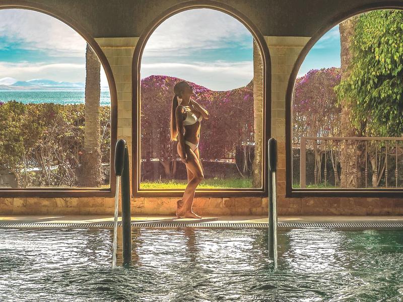 Piscine intérieure avec trois grandes fenêtres en arc offrant une vue sur la terrasse et le paysage.