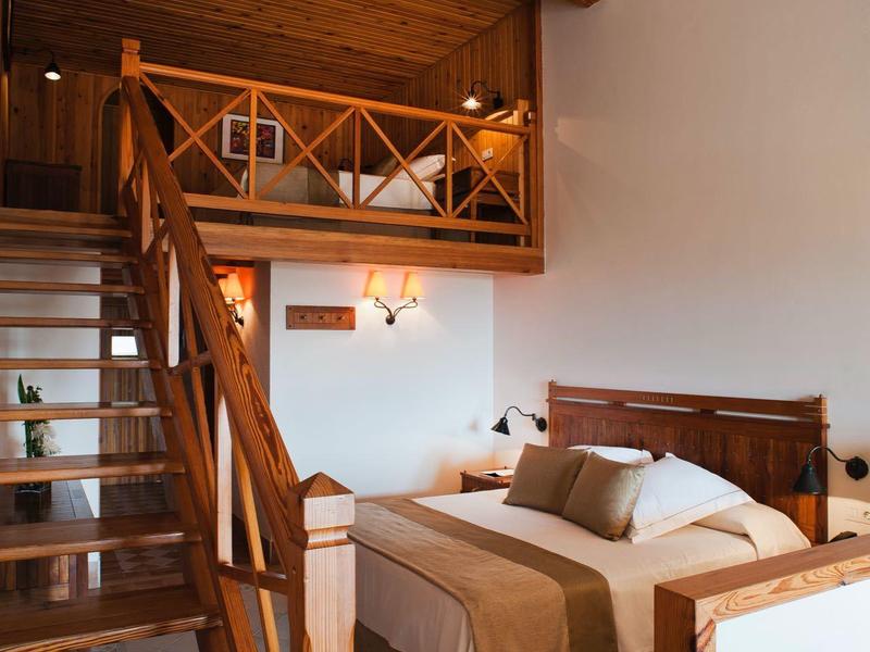 Chambre confortable avec poutres en bois, meubles en bois et escalier menant à une mezzanine.