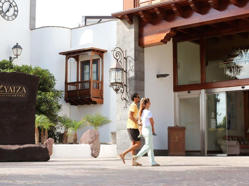 Deux personnes marchent devant un hôtel avec une façade blanche et des détails en bois.