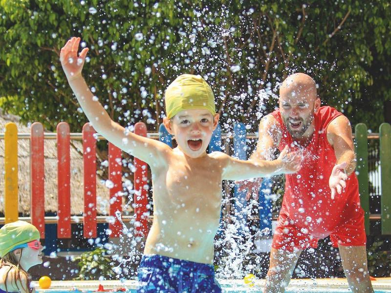 Un garçon et un homme jouent joyeusement dans une pataugeoire avec de l'eau éclaboussante.