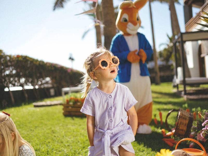 Enfant portant des lunettes de soleil et une robe au soleil avec une personne en costume de lapin en arrière-plan