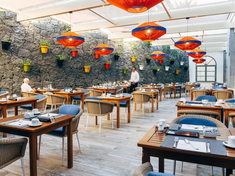 Restaurant moderne avec meubles en bois, lampes rouges et mur en pierre avec plantes.