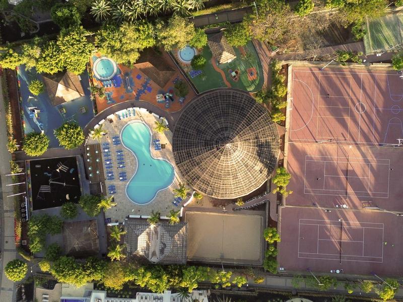 Vue aérienne d'un complexe hôtelier avec piscine, terrain de tennis et pavillon ombragé.