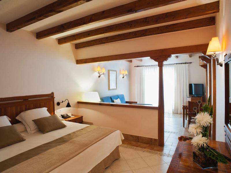 Chambre d'hôtel lumineuse avec lit double, poutres en bois et coin salon.