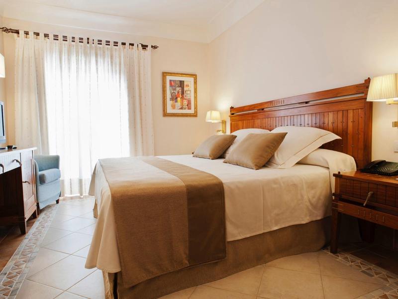 Chambre d'hôtel lumineuse avec lit double, meubles en bois et balcon avec rideaux