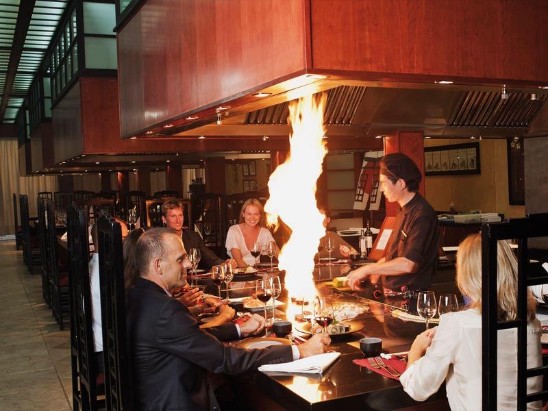 Des clients dégustent un repas au grill hibachi dans un restaurant à lambris en bois.