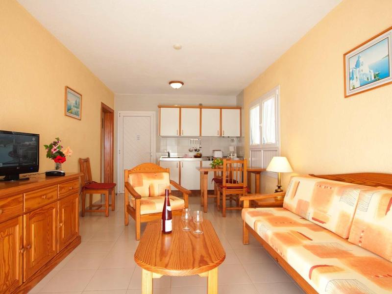 Bright living room with orange sofa, wooden table, and TV next to open kitchen.