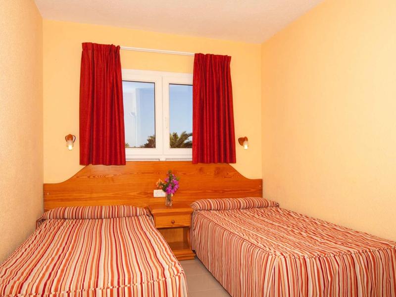 A simple hotel room with two single beds, orange walls, and red curtains.