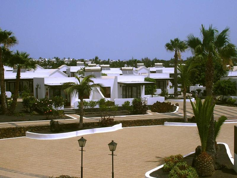 White flat-roofed buildings in a desert setting with palm trees under a clear sky.