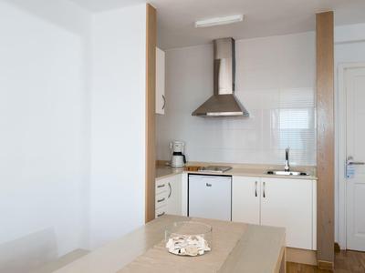 Kleine Küche mit weißen Schränken, Holzarbeitsplatte, Dunstabzugshaube und kleinem Kühlschrank.
