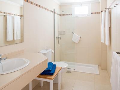 Helles Badezimmer mit ebenerdiger Dusche, großem Spiegel, Waschbecken und weißen Handtüchern.